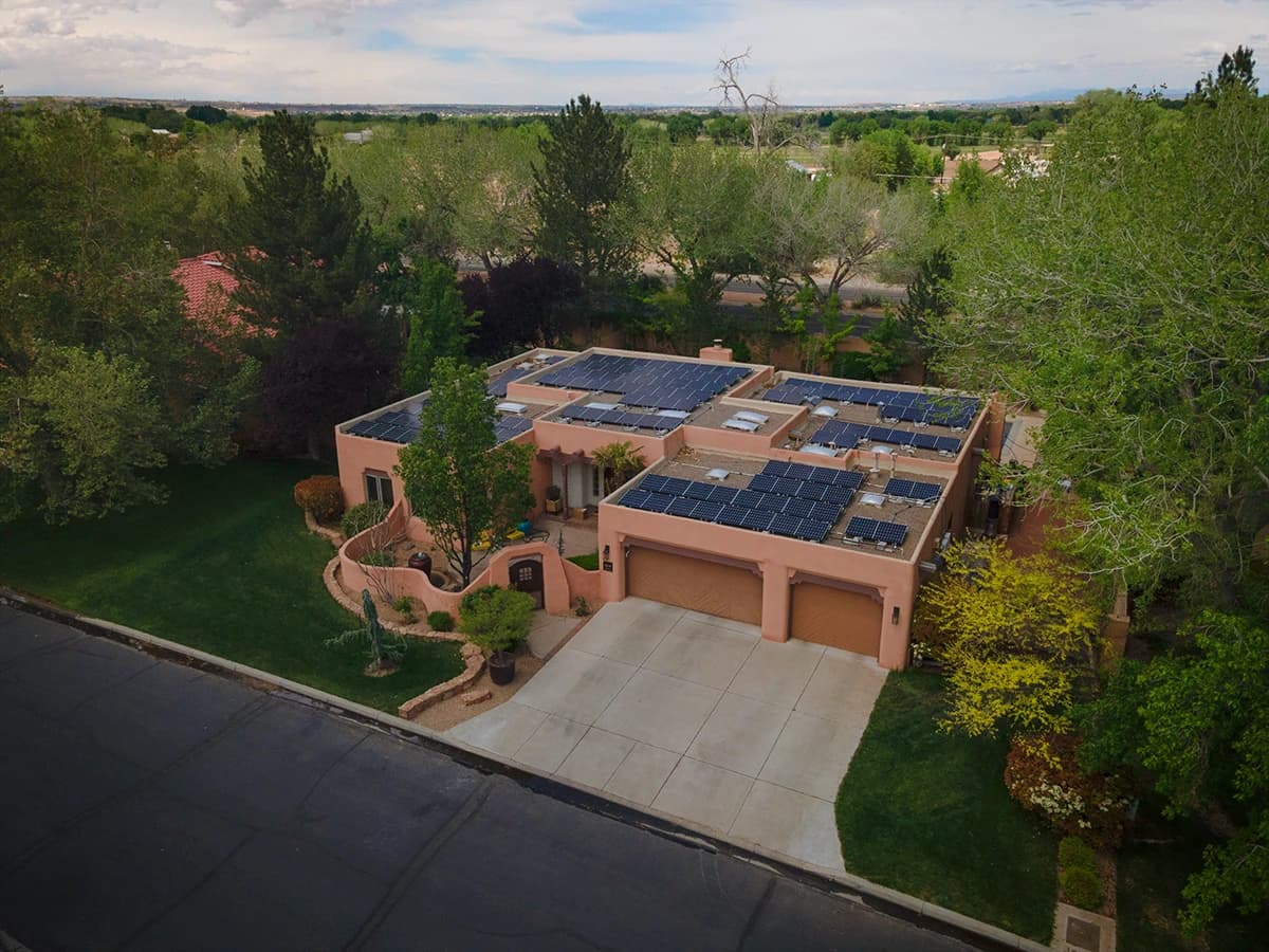A New Mexico stucco home surrounded by trees, with rooftop solar, flat roofs, and courtyard windows
